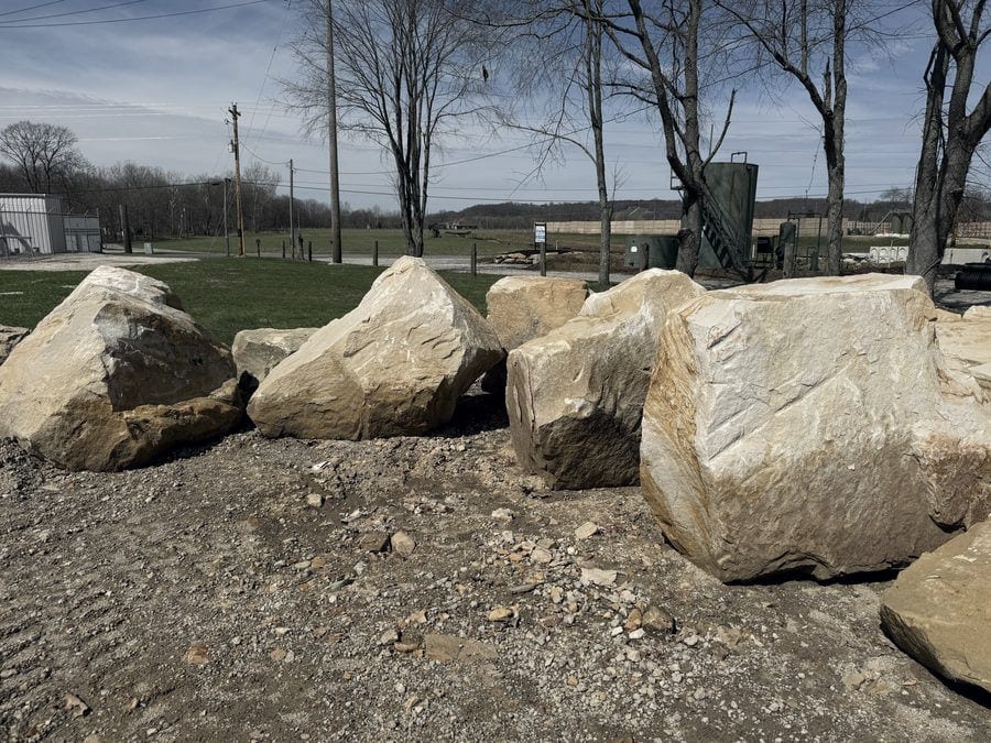 A row of large tan sandstone boulders laid out on the gravel at the supply yard.