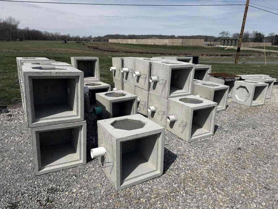 Precast concrete catch basins in several sizes lined up on the gravel at the supply yard.