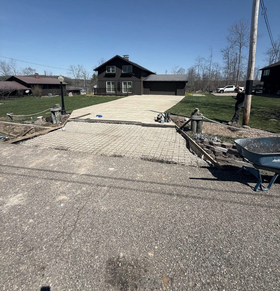The driveway during the pour, with wire mesh reinforcement laid out over the base and a wheelbarrow standing by at the road edge.