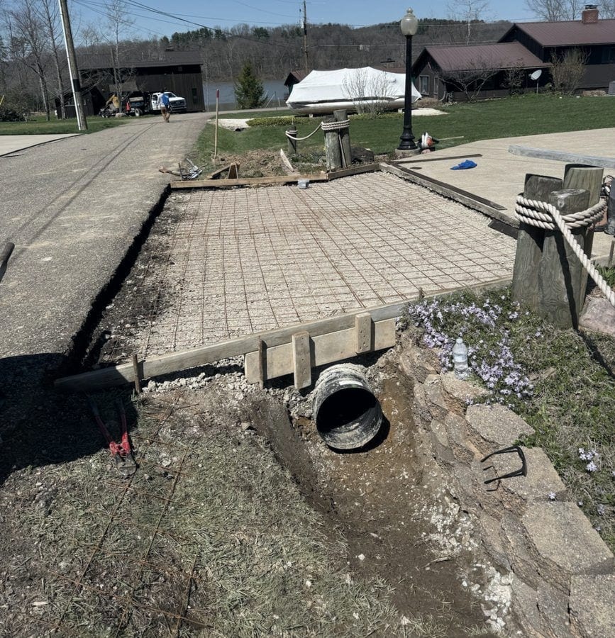 The old paver drive apron before the work, cracked and settled over an exposed culvert pipe, with a dry-laid stone headwall alongside.