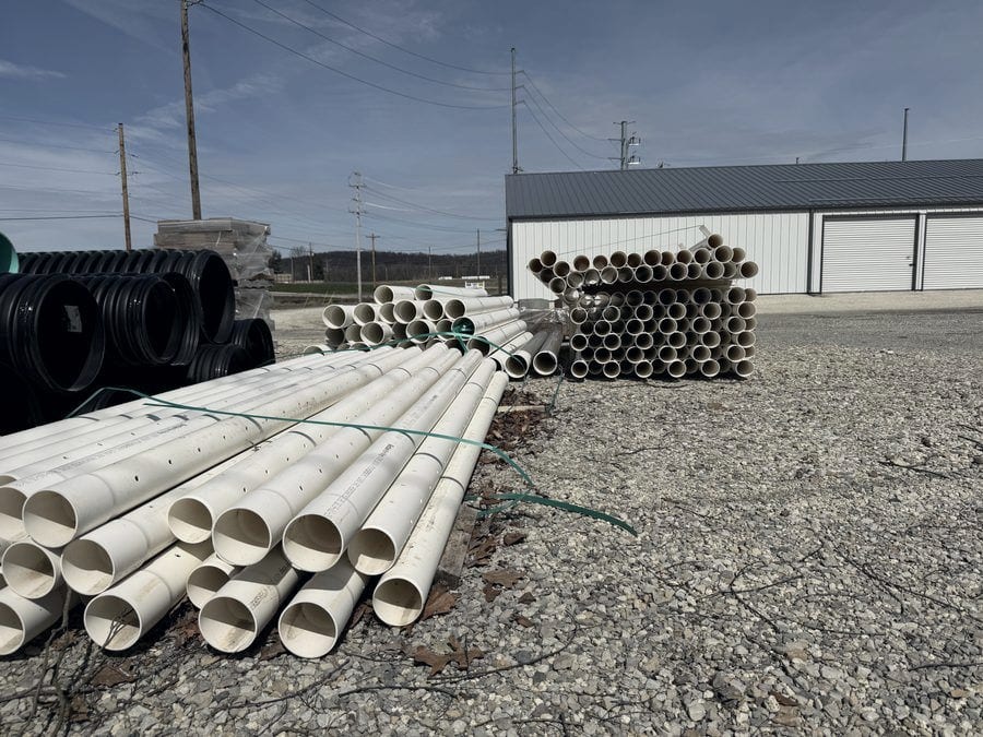 Bundles of white drainage pipe and coils of black corrugated pipe stacked in the supply yard.