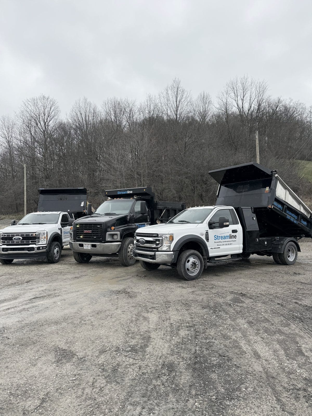 Three Streamline dump trucks parked together on gravel, the nearest one with its bed raised.