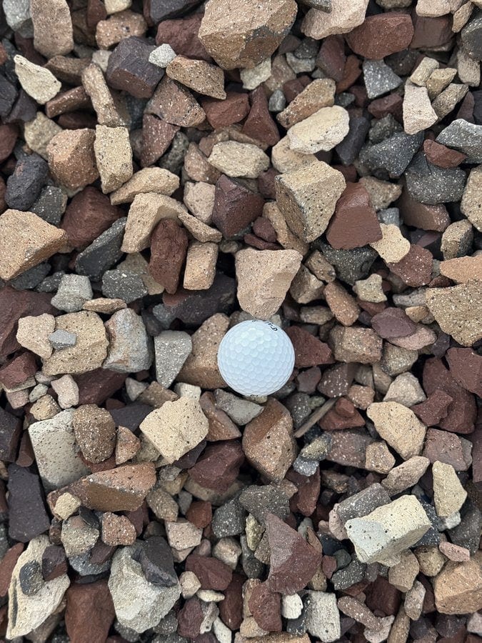 Multicolored crushed brick and stone in red, tan and gray, shown with a golf ball for scale.