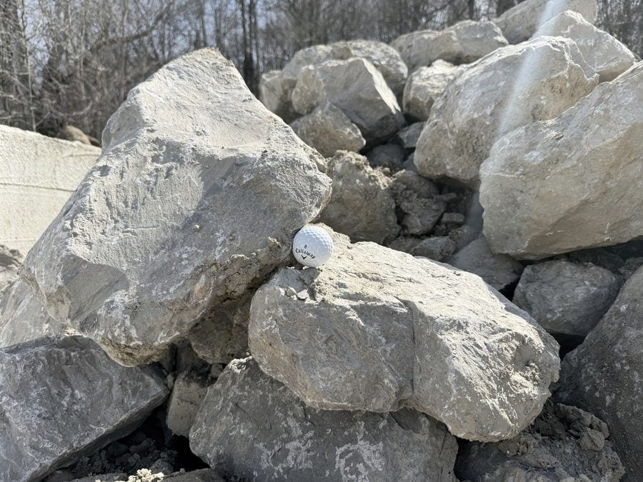 Large blocky cream limestone rip-rap, each piece many times the size of the golf ball wedged between them.