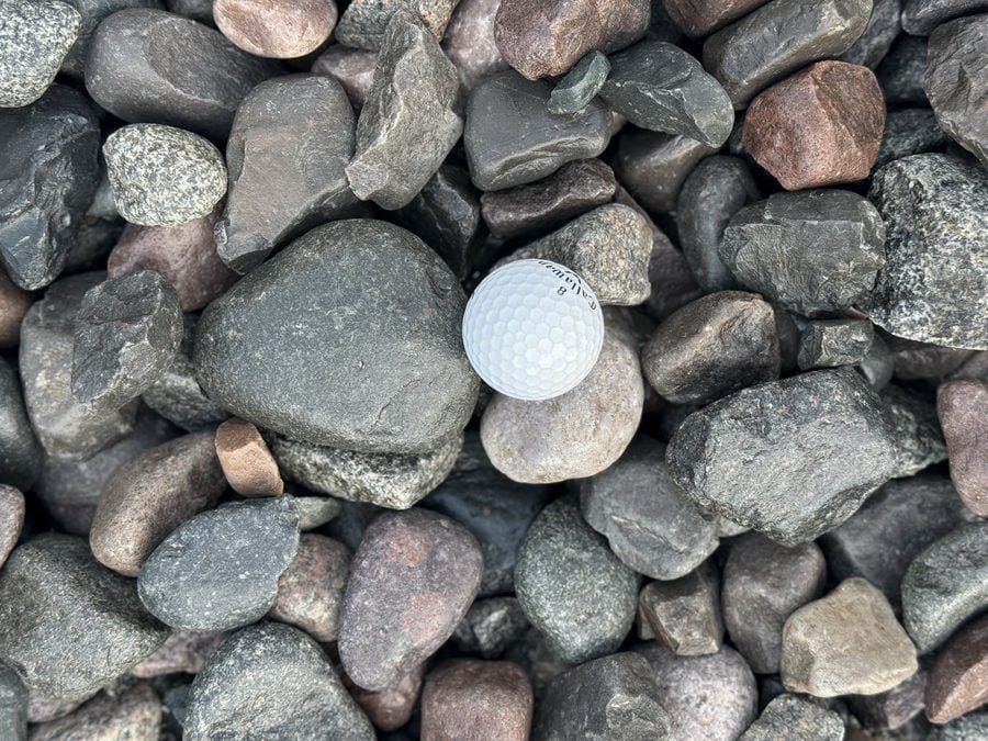 Large rounded river rock in blue-gray, green and red tones, most stones wider than the golf ball set among them.
