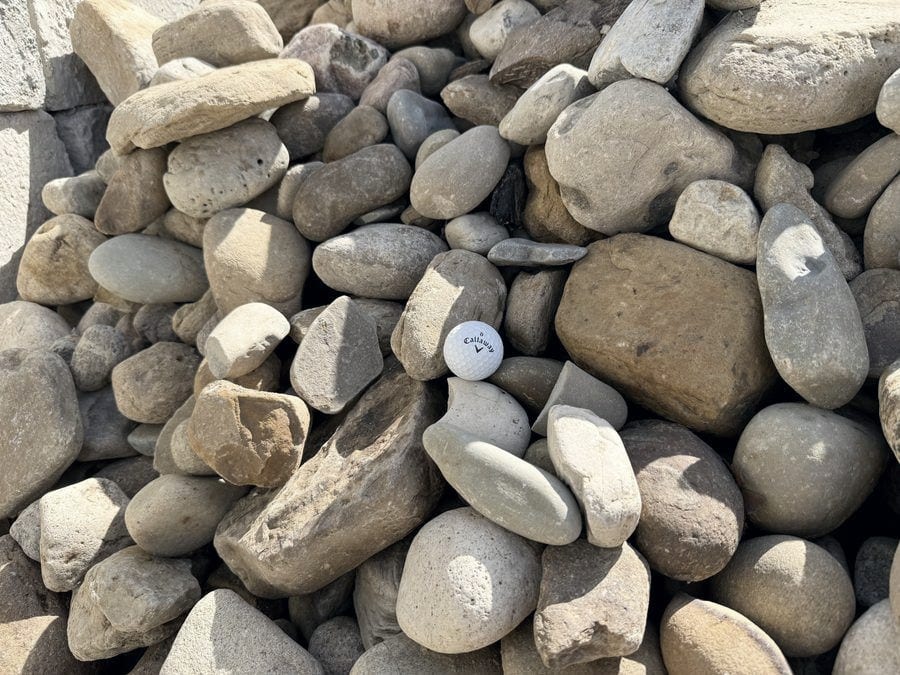 Large rounded river rock in tan, brown and gray, most stones bigger than the golf ball set among them.