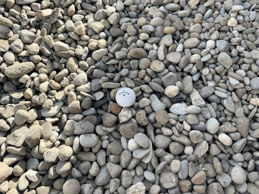 Small rounded tan and gray river gravel, far finer than the golf ball resting on it.