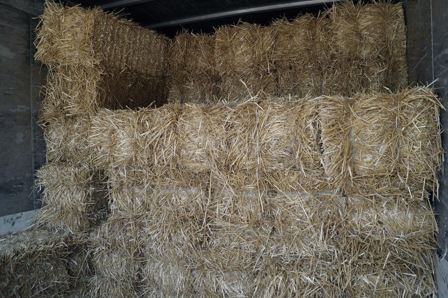 Straw bales stacked several rows deep under cover at the supply yard.