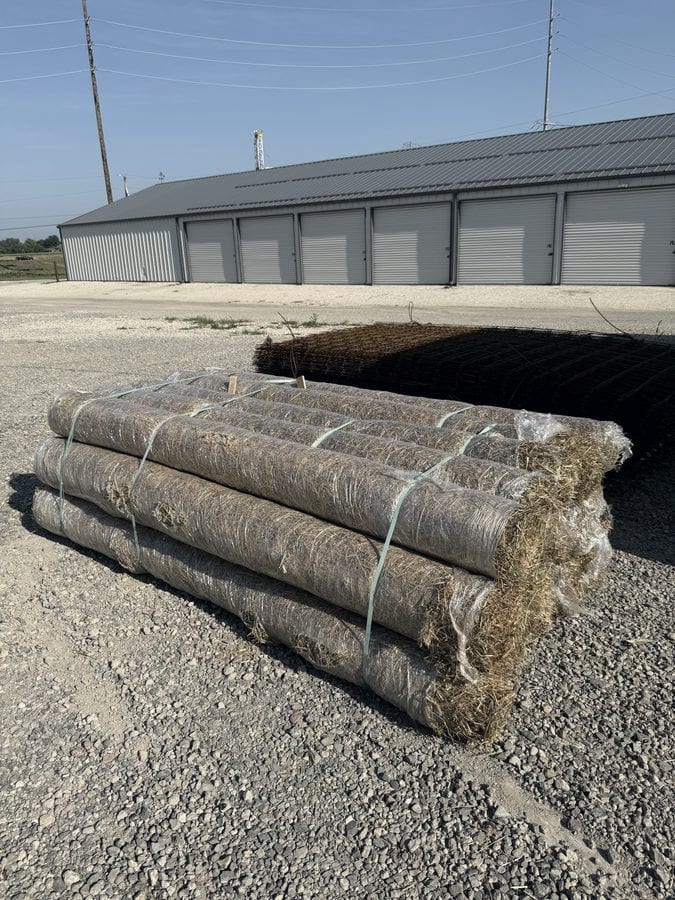 Rolls of straw erosion blanket stacked and banded outside the supply building.